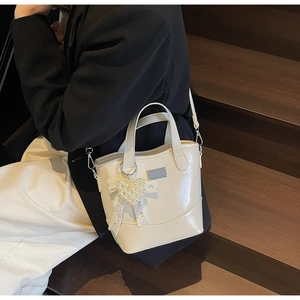 Detailed view of cream bucket bag with pearl heart charm and lace bow accessory