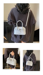 Detail view of the light grey glossy handbag with top handles and adjustable strap