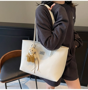White lychee texture tote bag with metal logo and cute plush bear charm on grey knitwear