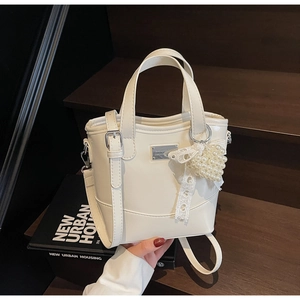 Detail view of a white bucket bag featuring a lace heart pendant and pearl decoration