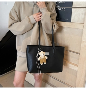 Close-up of black litchi pattern leather tote bag featuring a cute teddy bear charm