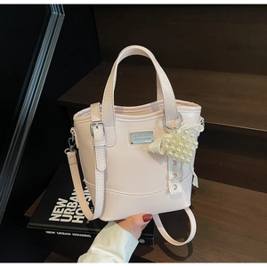 Detail of light pink bucket bag featuring a pearl heart charm and metal logo plaque