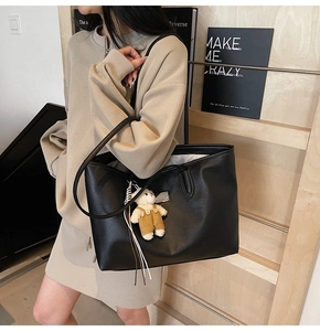 Detail of black pebbled leather tote bag with a cute plush bear charm on a slim strap