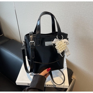 Detail of black patent leather bucket bag with pearl heart charm and lace bow accent