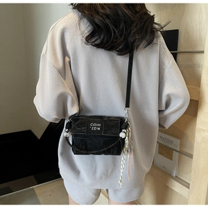 Detail shot of black woven crossbody bag featuring pearl charm and silk scarf decoration