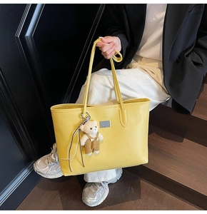 Detail of yellow pebbled leather tote bag with metallic plaque and cute plush bear charm