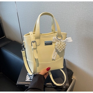 Detail of yellow bucket bag with pearl heart charm and lace bow on a soft leather surface