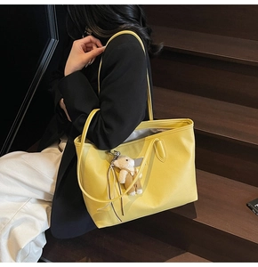 Detail of yellow pebbled leather tote bag with a cute brown bear charm on the shoulder strap