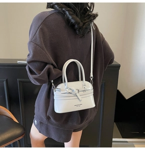 Close-up of minimalist light grey crossbody shell bag worn by model in vintage setting