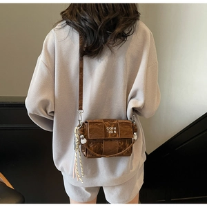 Detail of dark brown woven crossbody bag featuring a pearl pendant and fringe tassel