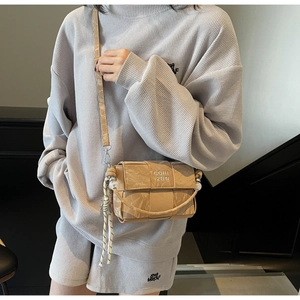 Close-up of beige woven crossbody bag with pleated texture and decorative pearl charm