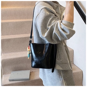 Detail of black glossy bucket bag with embossed logo and cartoon charm on strap