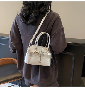 Detail of silver metallic crossbody shell bag showing adjustable strap and brand logo