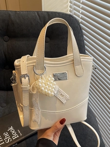 Minimalist beige bucket bag with pearl heart pendant and lace ribbon on a sofa