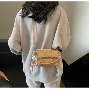Detail of khaki woven square crossbody bag featuring COIH 2DN text and tassel charm
