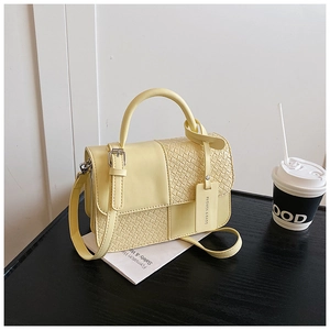Détail d'un sac à main carré jaune clair avec texture tressée et poignée sur table noire
