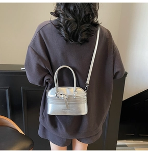 Model view of a metallic silver shell handbag with buckle detail and detachable strap