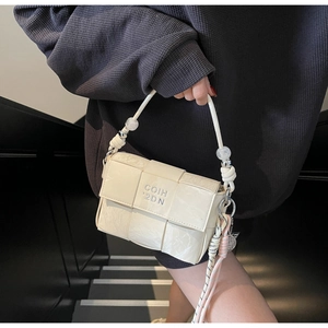 Close-up of woven cream handbag with beaded handle and decorative rope details