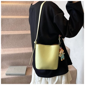 Side view of a yellow bucket bag with a cartoon doll charm on a model in a stairwell