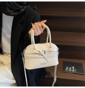 Detail showing creamy white shell bag with metallic buckle and branding logo on wood