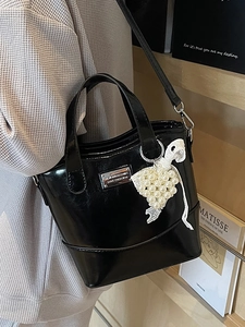 Chic black bucket bag with glossy finish featuring pearl bead and lace bow charm