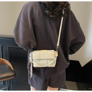 Detail of a creamy white woven crossbody bag featuring GOIH '2DN lettering on a model