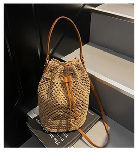 Detailed view of hollow woven straw bucket bag with brown leather drawstring closure