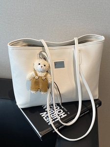 Minimalist white litchi pattern leather tote bag with a cute plush bear pendant on a chair