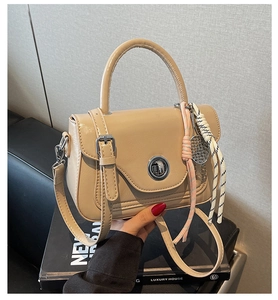 Detail view of the beige faux leather crossbody bag with metal twist lock and woven charm
