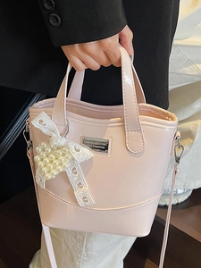 Pink patent leather bucket bag with pearl heart and lace bow charm held by a model