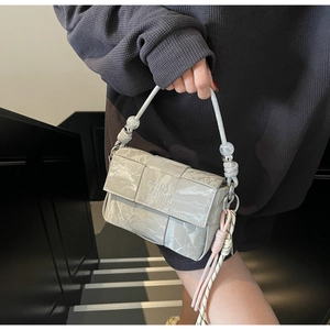 Close-up of woven handbag with bead handle and pink tassel charm in soft gray finish