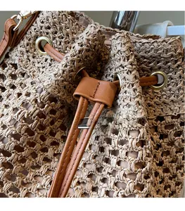 Detail of woven straw bucket bag with brown leather drawstring and gold metal eyelets