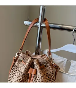 Close-up of khaki woven bucket bag with brown leather drawstring and reinforced bottom detail