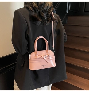 Rear view of model carrying pink shell-shaped handbag with bow and brand text detailing