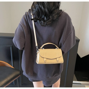 Vista dettagliata della borsa beige in pelle martellata indossata su maglione grigio