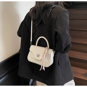 Beige oil wax leather crossbody bag shown on a black blazer with woven charm detail