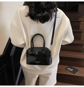 Rear view of a model carrying a black glossy shell bag with silver buckle detail