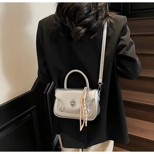 Close-up of a silver metallic crossbody bag with a round turn-lock clasp and a woven strap