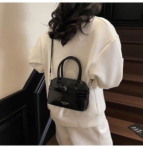 Detail of a black glossy shell bag featuring brand lettering and adjustable thin shoulder strap