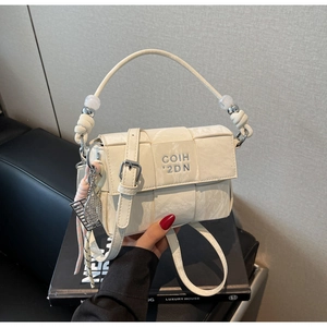 Detail showing cream woven texture, decorative pearl handle, and sports-style charm on bag
