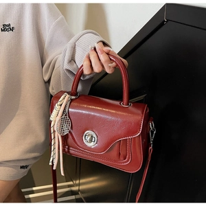 Detail of dark red oil wax leather handbag with silver twist lock and charm