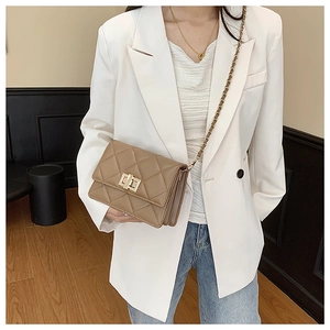 Détail du sac à bandoulière matelassé kaki avec fermoir doré sur un blazer blanc chic