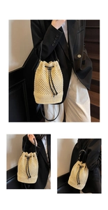 Close-up of beige hollow woven bucket bag with black drawstring closure and leather strap