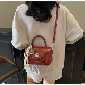 Detail of dark burgundy patent leather handbag with silver clasp and tennis racket charm