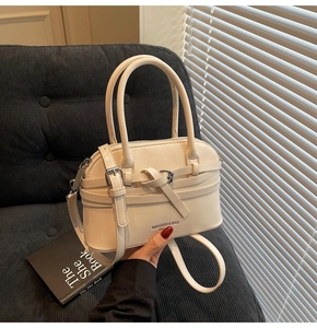 Close-up of cream shell handbag with top handles and logo detail on corduroy background