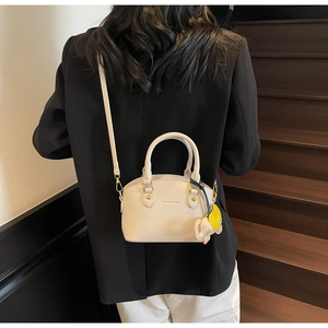 Detail of minimalist cream leather bucket bag with litchi texture and elephant charm