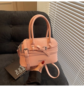 Detail of pink PU leather handbag with crisscross straps and silver buckles on a sofa