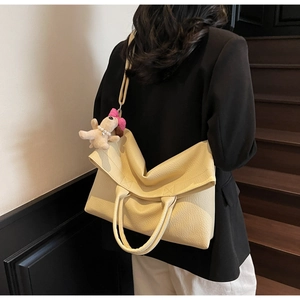 Vista detallada de bolso tote grande beige en cuero granulado con un colgante de peluche