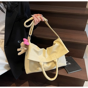 Detalle del bolso tote beige con textura de lichi y un colgante de perrito suave