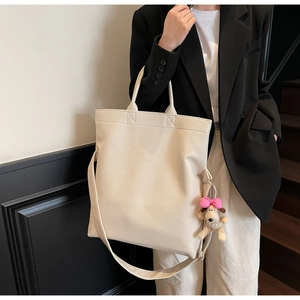 Detalle del bolso tote de cuero granulado crema con un colgante de perrito y bandolera